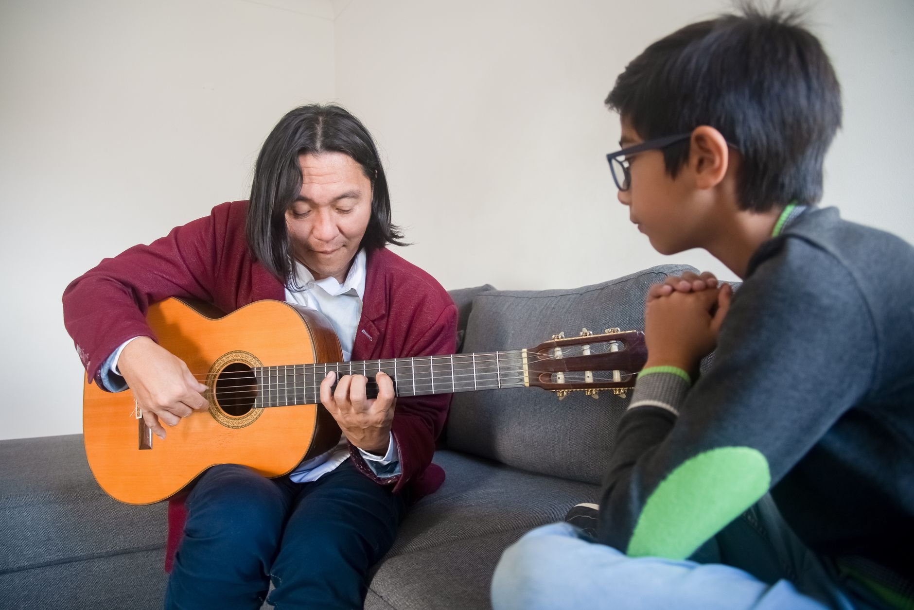 Acoustic guitar lesson with a teacher instructing a young student in a cozy indoor setting